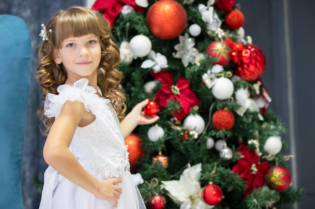 A beautiful child decorates a Christmas tree Elegant girl in christmas time