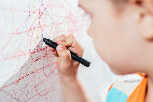 Beautiful child draws on the wall with colored pencils