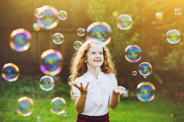 Beautiful child enjoying blowing soap bubbles in the summer on nature. 