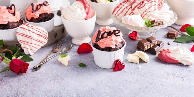 Beautiful chocolate cupcake, pink cream, meringue cookies and red roses on gray stone surface. Valentines, Mother Day, wedding concept with copy space