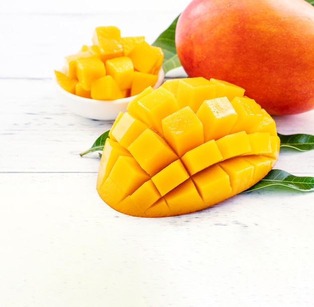 Beautiful chopped mango chunks with green leaves on bright white color timber background Copy space close up macro Tropical fruit concept