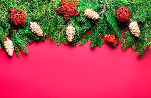 A beautiful Christmas garland made of fir trees with red Christmas balls and golden cones on a red background Festive concept with copy space