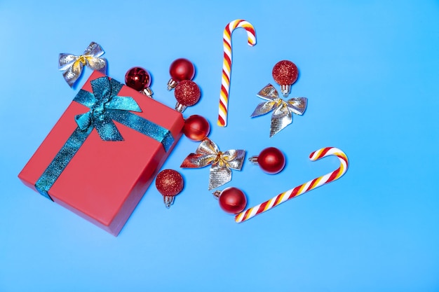 Beautiful Christmas red balls and a red gift with a green ribbon with lollipops on a blue background New year christmas concept Flat lay festive mockup with copy space