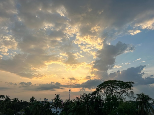 Beautiful cloudy sky and sunset view in a rural area Scenic sunset view with thick clouds and sunbeams coming out from the clouds Twilight time sky scenery with trees and dark clouds