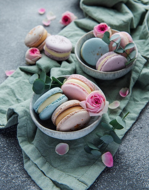 Photo beautiful colorful tasty macaroons and pink roses on a concrete background