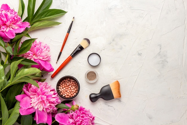 Beautiful composition of decorative cosmetics  with pink peonies. Top View.