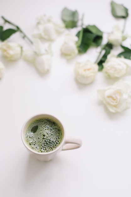 Beautiful composition with cup of green matcha tea and roses on white background