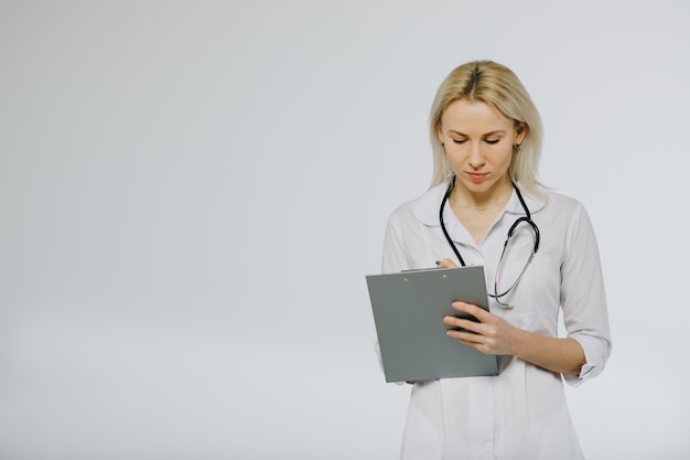 Beautiful confident female doctor in white medical coat and stethoscope looking calm on clipboard with patients medical history. Copy space. Clinic ads and offers.