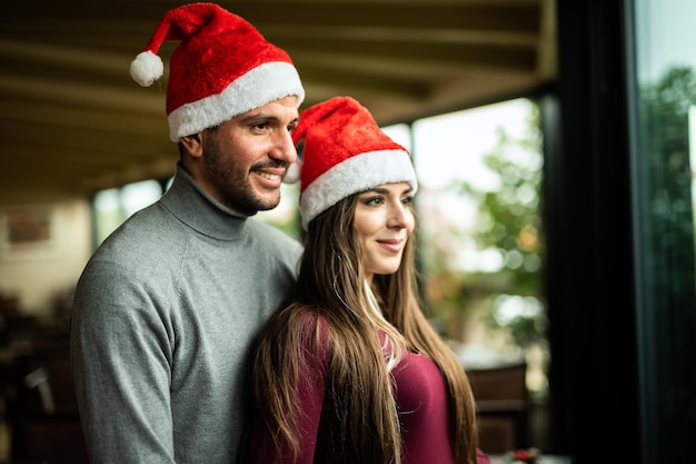 Beautiful couple hugging wearing Santa hats near a window