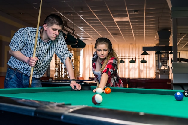 Beautiful couple playing billiard in night pub