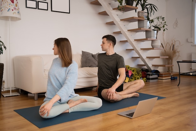 Beautiful couple practicing yoga together at home using a laptop taking online yoga classes