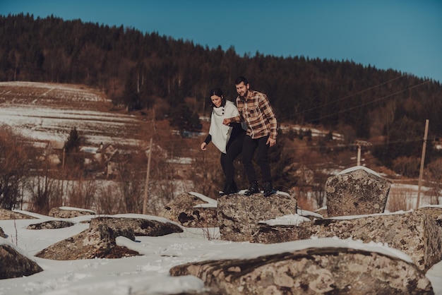 Beautiful couple in winter nature walking the rocks covered by snow against a cloudless sky and bare trees Selective focus