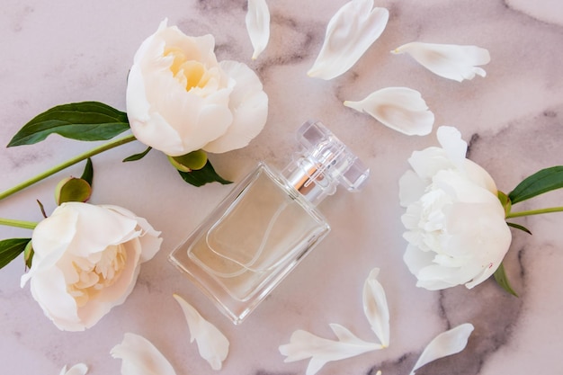 A beautiful crystal bottle of women's perfume or toilet water on a marble background among white peonies aroma attraction top view