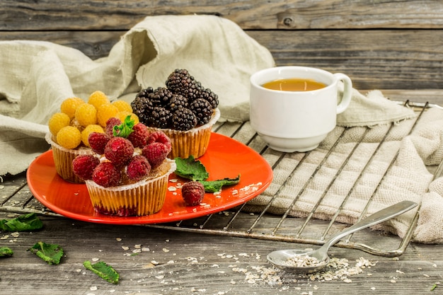 beautiful cupcakes with berries on wooden background in red plate