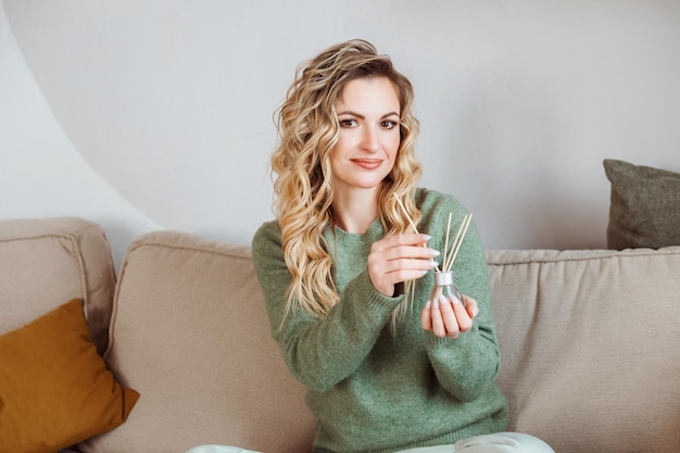 Beautiful curly blonde woman holding aroma diffuser home fragance in her hands