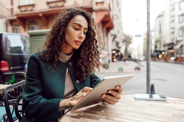 Beautiful curly businesswoman using digital tablet outdoors in cafe