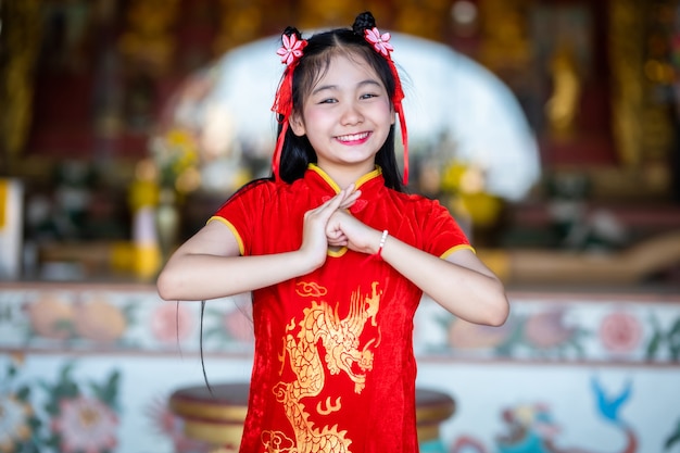 Beautiful Cute little Asian young woman wearing red traditional Chinese cheongsam, Stand for pray to buddha statue for Chinese New Year Festival at Chinese shrine