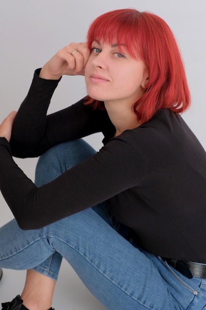 Beautiful cute young woman with orange hairstyle in jeans sitting posing in studio on white background