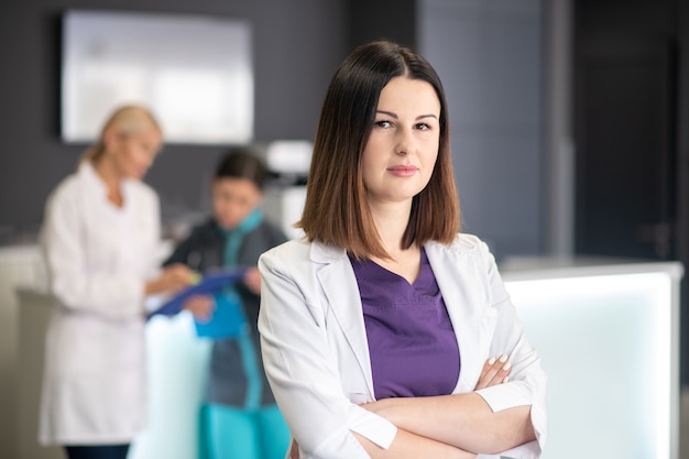 Beautiful dark-haired doctor wearing white robe looking serious