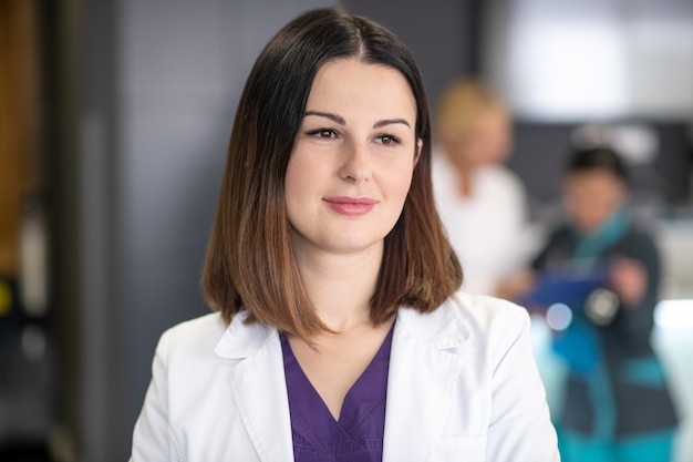 Beautiful dark-haired doctor wearing white robe looking thoughtful