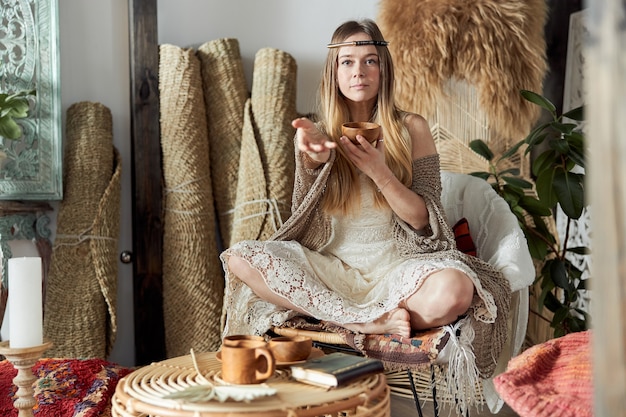 Beautiful dark haired woman in shamanic ethnic outfit in bali style decorated room