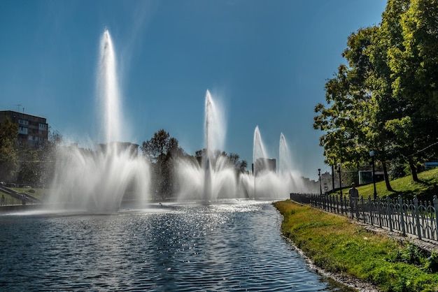 A beautiful day in the public park Blue clear sky fountains on the pond green trees and grass