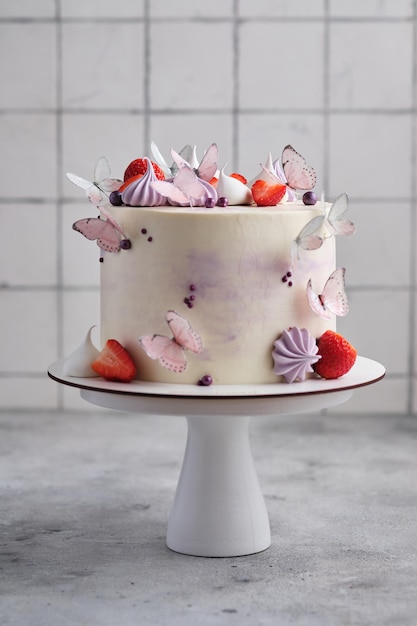 Beautiful and delicate strawberry cake for a girl. Dessert is decorated with fresh strawberries, meringues and butterflies.