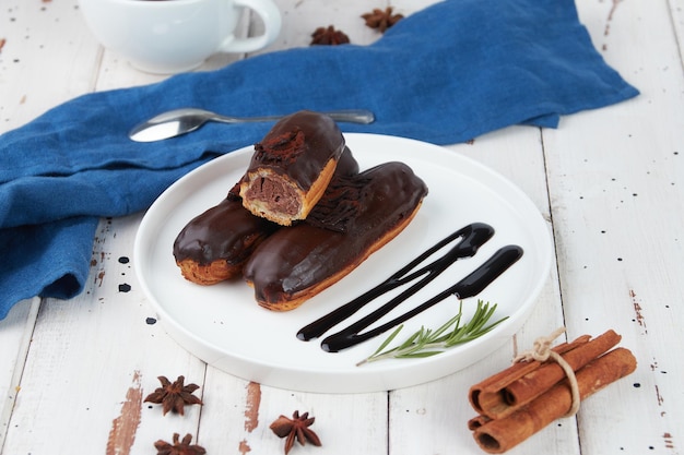 Beautiful delicious french eclairs set with original cream decor on white plate on wooden background tasty colorful dessert profiteroles