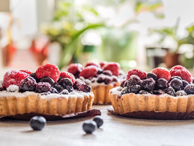 Beautiful delicious tarts, colorful pastry cakes sweets with fresh raspberries and blueberry on white wooden background.