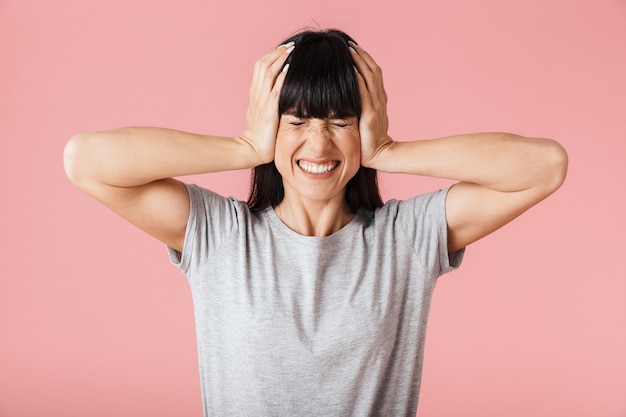 a beautiful displeased woman posing isolated over light pink wall wall covering ears.