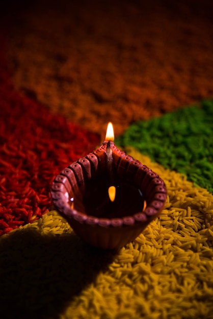 Beautiful Diwali Greeting using Diya or clay oil lamp lit and arranged over Rangoli made by multi coloured rice grains, selective focus