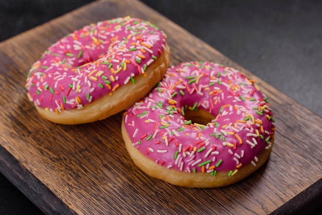 A beautiful doughnut with pink glaze and colored sprinkle on a dark concrete background