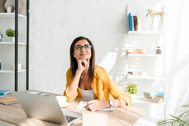 Beautiful dreamy freelancer working with laptop in home office