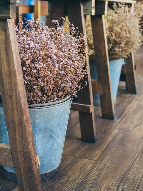 Beautiful dried flowers in metal bucket under the wooden table on wooden floor