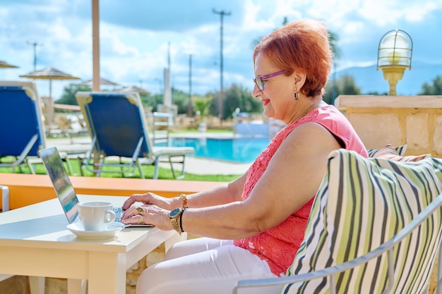 Beautiful elderly pension age woman sitting outdoor with laptop