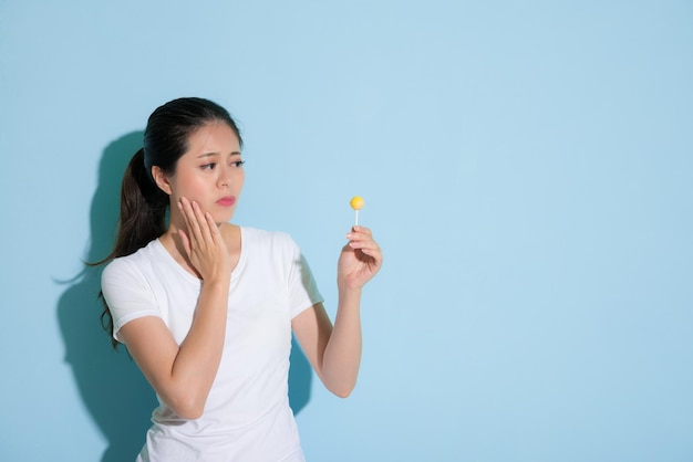 beautiful elegant girl looking at lollipop candy thinking about teeth health care worry about tooth decay standing on blue wall background.