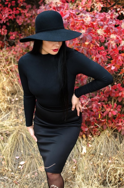 Beautiful elegant woman in a black hat standing in a park in autumn