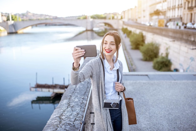 Beautiful and elegant woman making selfie photo standing near the river in Lyon old town during the morning