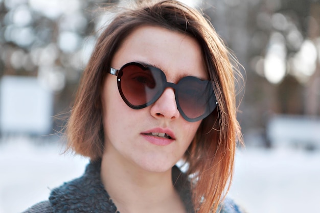 Beautiful elegant woman in a sweater and heart-shaped sunglasses in winter