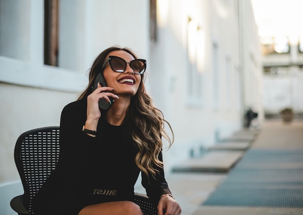 Beautiful elegant woman with sunglasses talking on the phone. Girl sitting with cell phone.
