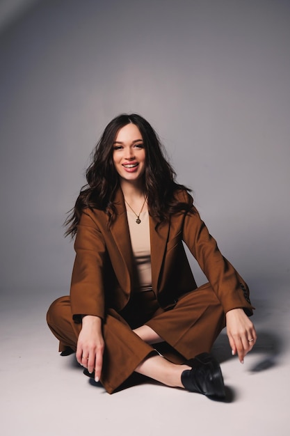 Beautiful elegant young woman model in nice stylish brown suit posing on gray background Young elegant woman in a suit