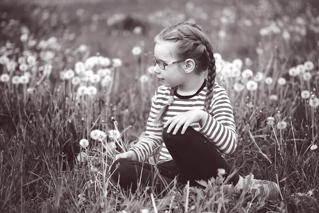 Beautiful emotional girl with glasses playing with dandelions childhood concept