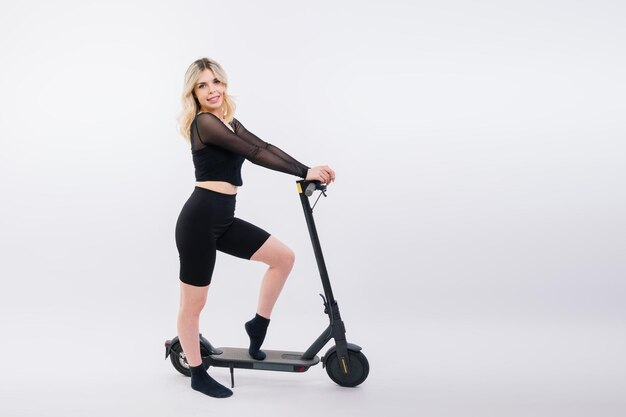 Beautiful emotional young female in sport clothes on electric scooter on red and white background