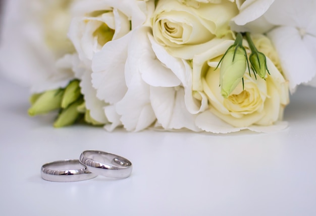 Beautiful engagement rings and bridal bouquet of white flowers on a white surface