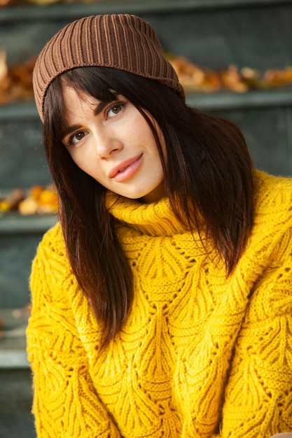 Beautiful European brunette dressed in a yellow woolen sweater and hat outside