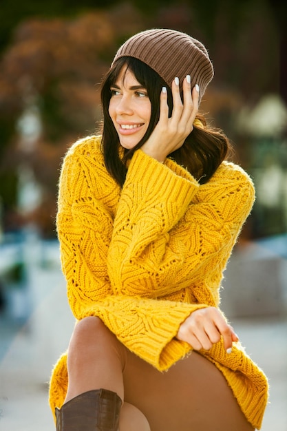 Beautiful European brunette dressed in a yellow woolen sweater and hat outside