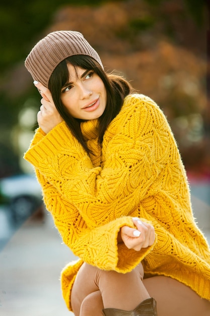 Beautiful European brunette dressed in a yellow woolen sweater and hat outside