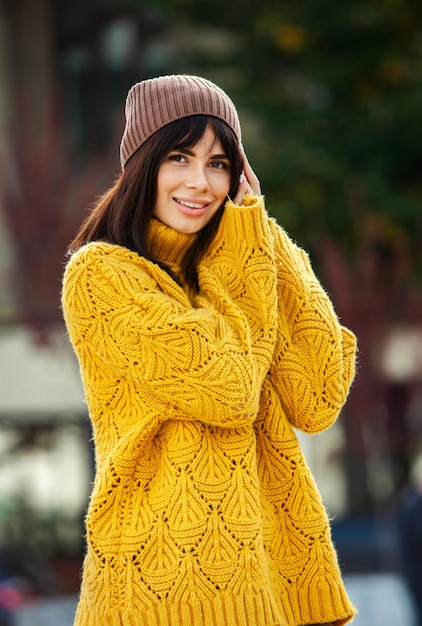 Beautiful European brunette dressed in a yellow woolen sweater and hat outside