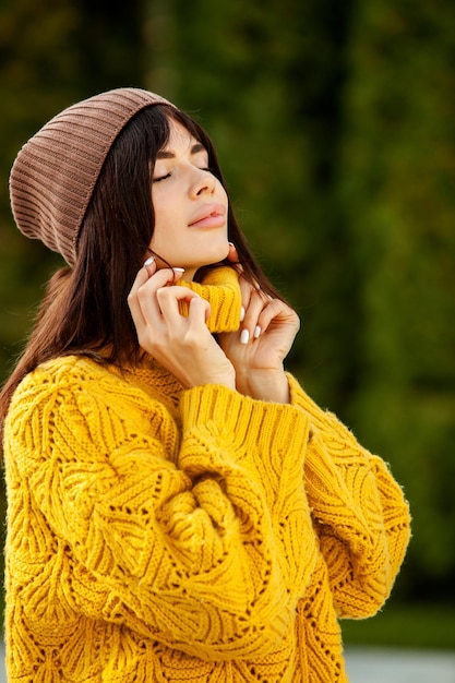 Beautiful European brunette dressed in a yellow woolen sweater and hat outside