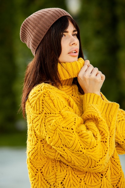 Beautiful European brunette dressed in a yellow woolen sweater and hat outside